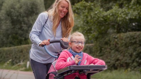 Een lachende moeder duwt haar lachende dochter vooruit in een rolstoel